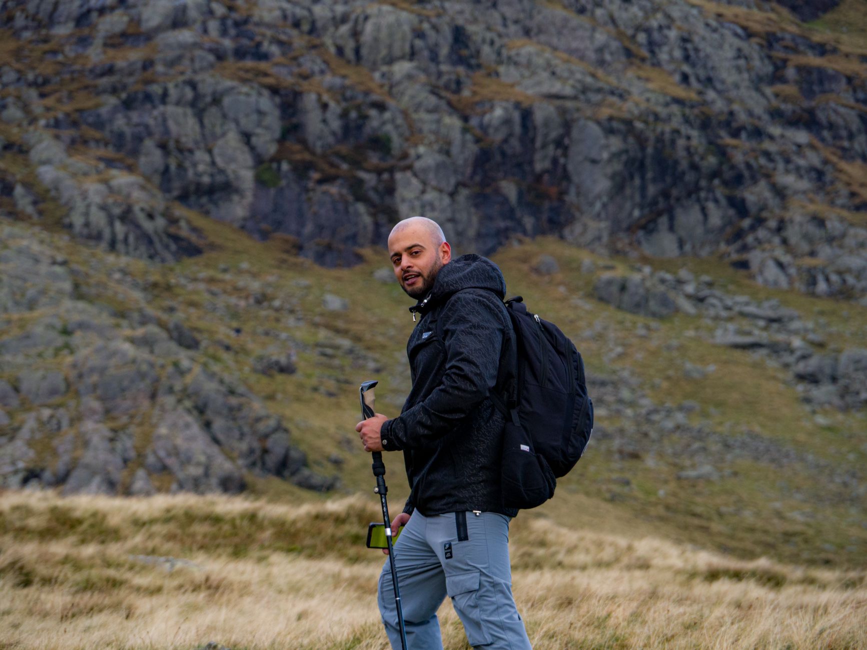 Turysta z plecakiem i kijem trekkingowym na skalistym szlaku w górach