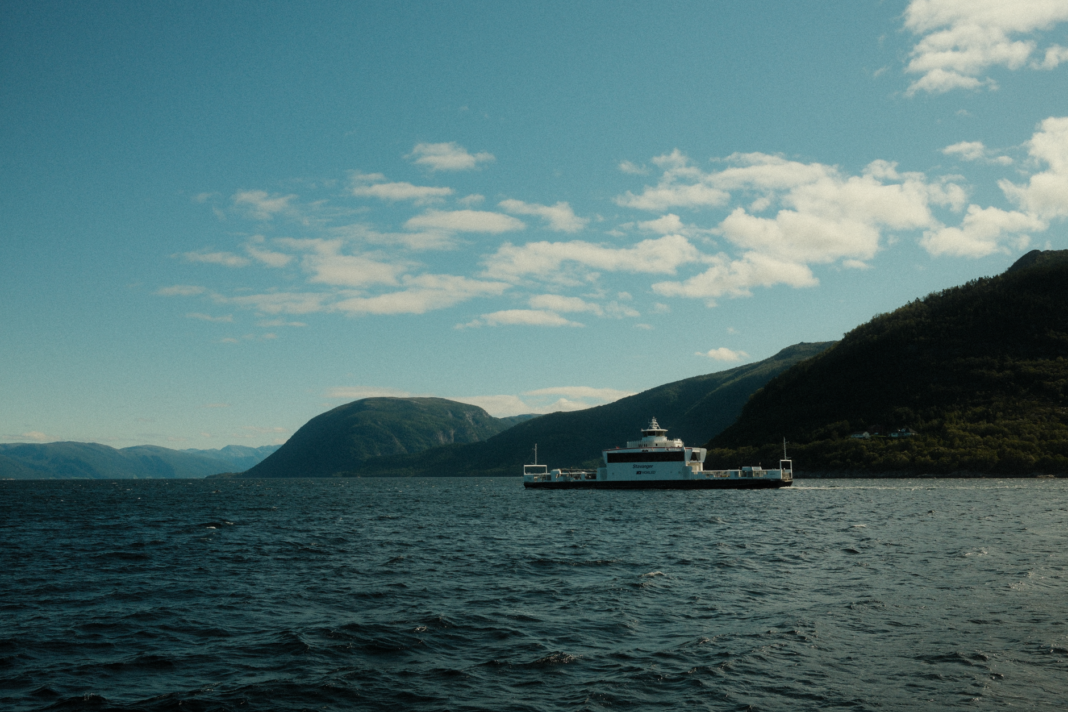 Prom pasażerski płynący przez norweski fiord pod błękitnym niebem Prom pasażerski płynący przez norweski fiord pod błękitnym niebem